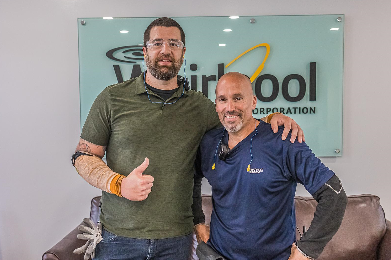 Two gentleman standing together in front of Whirlpool Corporation logo sign.