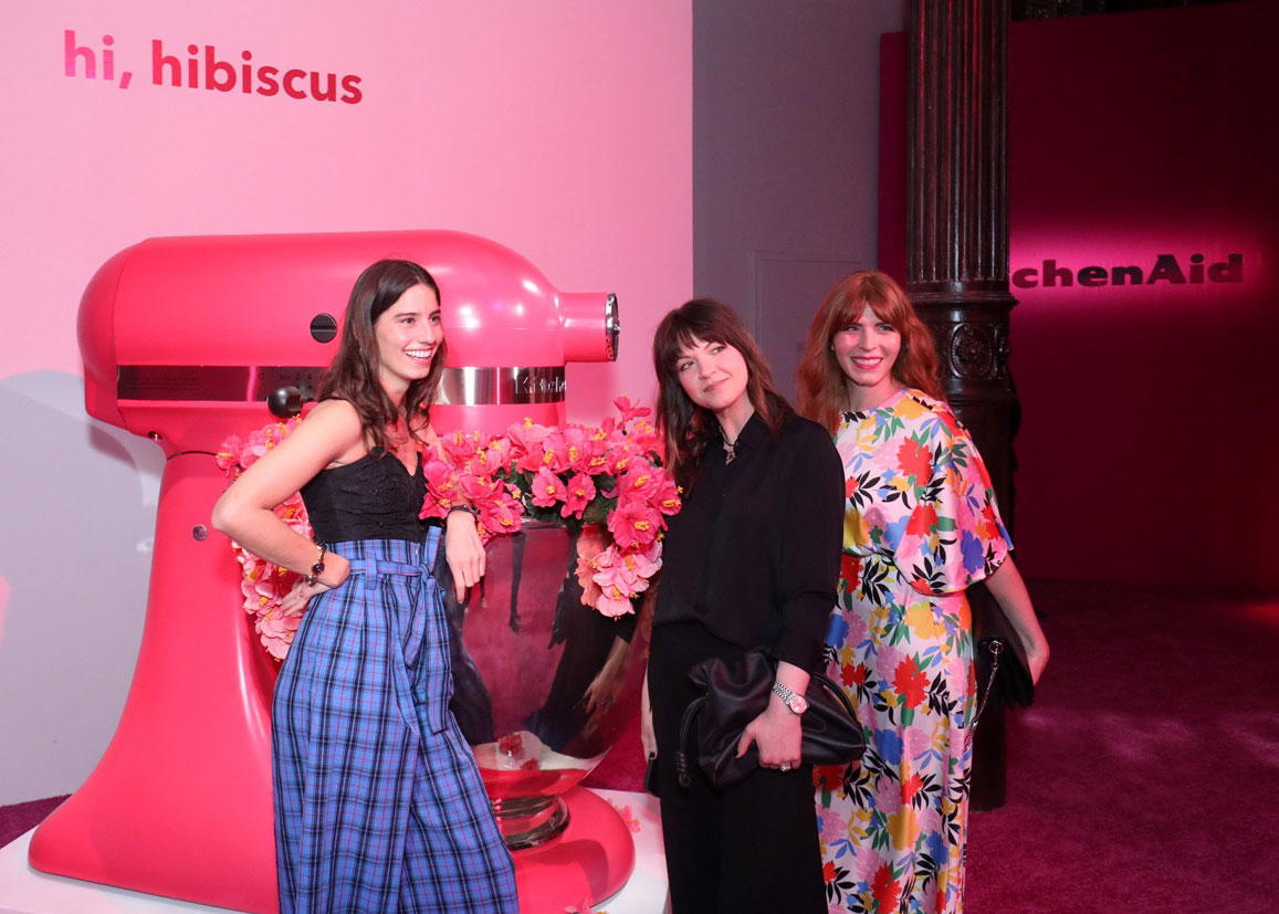 Three designers from the KitchenAid brand team stand in font of a giant stand mixer
